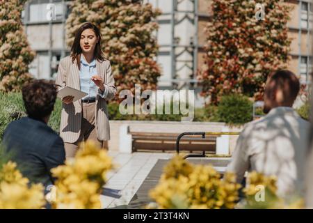 Femme cadre expliquant la nouvelle stratégie marketing à ses coéquipiers tout en travaillant à distance dans la ville Banque D'Images