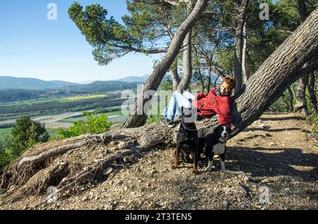 Femme métis ayant un repos sur un tronc d'arbre incliné tout en promenant ses chiens au sommet des 'Pénitents', formations rocheuses de 100 mètres de haut surplombant le village de les Mées et ses environs. Alpes de haute Provence, France. Banque D'Images