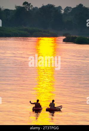 Silhouettes de deux figures humaines en kayaks, dérivant à travers les eaux calmes et paisibles du Mékong, à travers des rayons de lumière dorée réfléchis sur l'eau, Banque D'Images