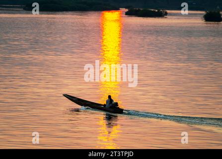 Silhouette de la figure humaine dans le petit bateau Motot étroit, dérivant à travers les eaux calmes et pacifiques du Mékong, à travers des rayons de lumière dorée réfléchis sur Banque D'Images