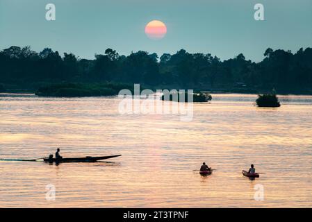 Silhouettes de figures humaines dans de petits bateaux,dérivant à travers les eaux calmes, paisibles du Mékong,à travers des rayons de lumière dorée réfléchis sur l'eau Banque D'Images