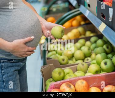 La femme enceinte choisit des pommes dans le magasin. Banque D'Images