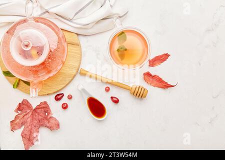 Réglage de table d'automne avec théière en verre et tasse de thé aux baies bio avec du miel parmi les feuilles. Espace de copie. Banque D'Images