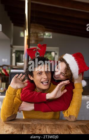 Portrait d'heureux couple masculin gay diversifié portant des chapeaux de noël et ayant un appel vidéo à la maison Banque D'Images
