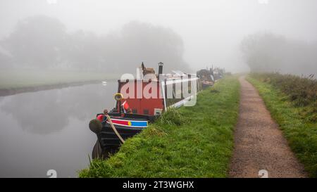 En regardant le chemin de halage d'un canal dans un matin brumeux. Il y a une rangée de bateaux étroits amarrés sur le côté du canal Banque D'Images