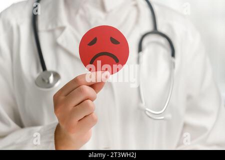 Gros plan d'une jeune femme médecin en uniforme blanc avec stéthoscope tenant une émoticône rouge en colère. Intelligence émotionnelle, équilibre le contrôle des émotions, moi Banque D'Images