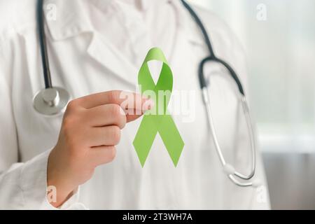 Gros plan d'une jeune femme médecin en uniforme blanc et stéthoscope tenant un petit ruban vert. Journée mondiale bipolaire. Journée de sensibilisation à la santé mentale, Dépression Banque D'Images