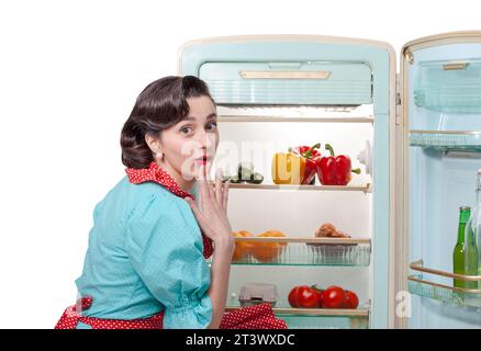 Femme au foyer de style vintage dans la cuisine préparant le déjeuner, elle ouvre le réfrigérateur et regarde la caméra Banque D'Images