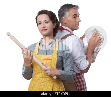 Forte femme souriante avec rouleau à regarder son mari la vaisselle Banque D'Images