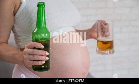 Femme enceinte tenant verre et bouteille de bière. Banque D'Images