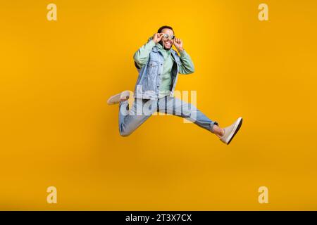 Photo pleine longueur de beau gars cool hispanique courir sautant touchant son Sunglass positive profiter de la vente isolé sur fond de couleur jaune Banque D'Images