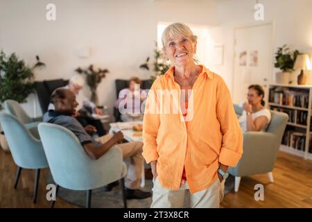 Portrait de femme âgée retraitée souriante debout avec les mains dans les poches à la maison de retraite Banque D'Images