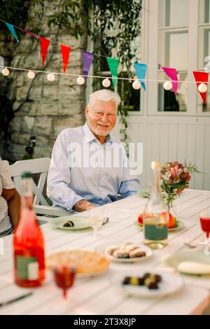 Portrait d'un homme âgé souriant assis à la table à manger dans la cour arrière Banque D'Images