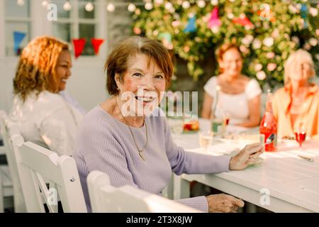 Portrait de femme âgée heureuse assise à la table à manger dans la cour arrière Banque D'Images