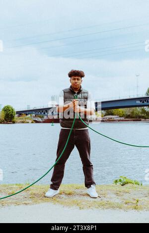 Portrait en longueur d'un jeune homme confiant tenant le tuyau d'arrosage près de la rivière Banque D'Images