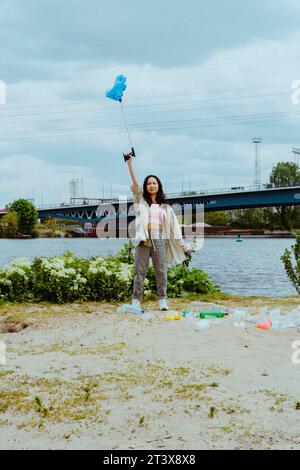 Portrait en longueur d'une jeune femme confiante ramassant des ordures près de la rivière Banque D'Images