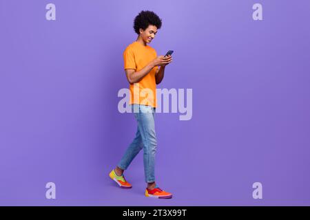 Pleine longueur cadre de jeune gars négociant bitcoin emoney en ligne porter tenue décontractée millionnaire utiliser le téléphone isolé sur fond de couleur violette Banque D'Images