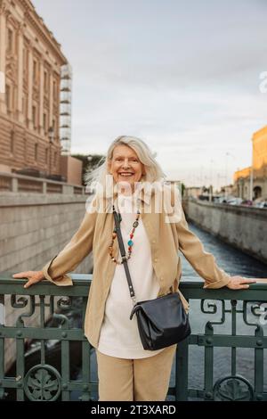 Portrait de femme aînée souriante appuyée sur la rampe au-dessus du canal Banque D'Images