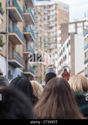 Merida, Espagne - 10 décembre 2022 : une femme lève le bras pour enregistrer avec son smartphone la procession Eulalia de Mérida. Martyr vénéré avec grand dev Banque D'Images