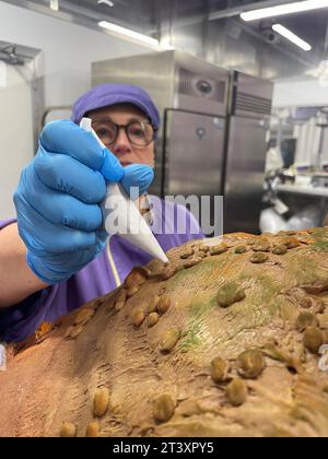 La chocolatière Donna Oluban apporte la touche finale à un présentoir d'Halloween avec un crapaud effrayant aux feuilles d'automne, une baguette et des livres de sorts faits de chocolat au Cadbury World de Birmingham. La création détaillée de 90 cm de haut, comprenant 50 kilogrammes de chocolat, a été conçue pour être «aussi fantaisiste que possible sans être trop effrayante» pour les visiteurs de l'attraction de Birmingham. Date de la photo : mercredi 25 octobre 2023. Banque D'Images