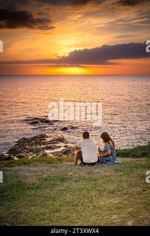 Vacanciers assis sur la côte et profitant d'un coucher de soleil spectaculaire sur la baie de Fistral à Newquay, en Cornouailles, au Royaume-Uni, en Europe. Banque D'Images