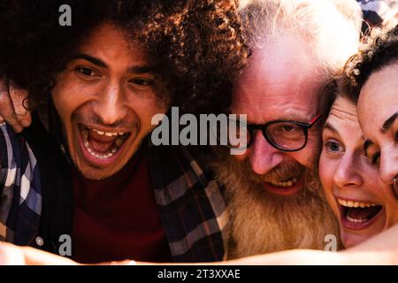 Un ensemble animé d'amis, variant en âge, sexe et race, se rapprochent, leurs têtes se blottirent dans un cercle de camaraderie. L'air bourdonne de rire alors qu'ils font des visages drôles, capturant un selfie spontané rempli de joie intacte et d'inclusivité. La scène est un délicieux instantané de l'amitié moderne, où la diversité est célébrée, et chaque moment est mûr pour le rire partagé. Playful Melting Pot divers amis partagent un joyeux moment Selfie. Photo de haute qualité Banque D'Images