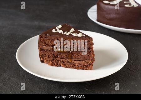 Gâteau au chocolat Sacher avec confiture d'abricot sur plaque blanche. Dessert autrichien traditionnel. Arrière-plan sombre. Banque D'Images