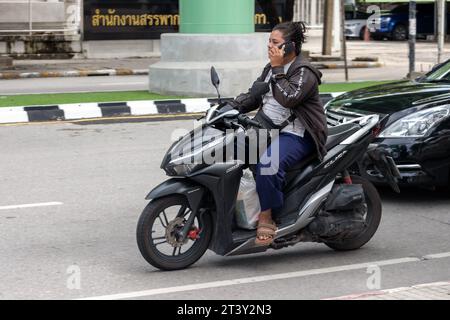 SAMUT PRAKAN, THAÏLANDE, octobre 11 2023, Une femme conduit une moto et appelle sur un téléphone portable Banque D'Images