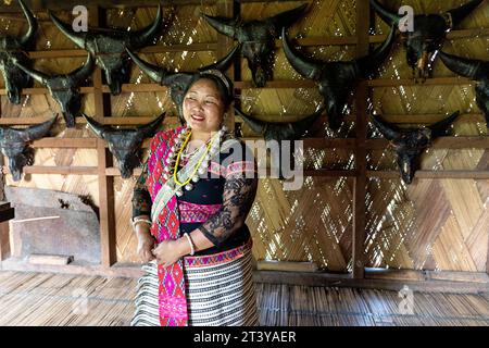 Femme de la tribu Adi en vêtements adi traditionnels posant dans une maison traditionnelle en bois avec des murs décorés de crânes de taureau en Assam dans le nord-est de l'Inde Banque D'Images