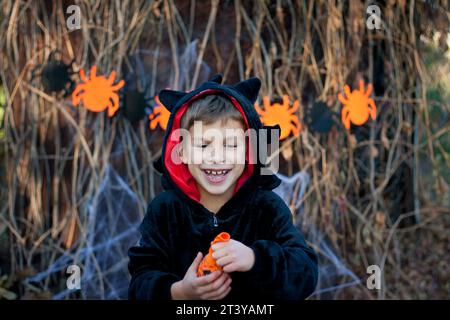 Joyeux Halloween. Portrait de garçon d'âge préscolaire heureux en costume de carnaval de dragon noir. enfant s'amusant, ballon gonflant. Fête d'Halloween en plein air, autum Banque D'Images