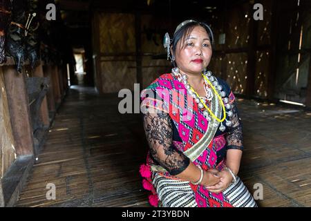 Femme de la tribu Adi en vêtements traditionnels assis devant le mur décoré avec des têtes de taureau dans une maison traditionnelle en bois à Assam, dans le nord-est de l'Inde Banque D'Images