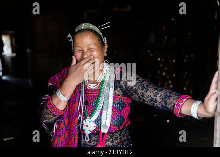 Femme de la tribu Adi en vêtements traditionnels souriant avec la main sur la bouche, appuyée sur la porte ouverte dans une maison traditionnelle en bois à Assam dans le nord-est de l'Inde Banque D'Images