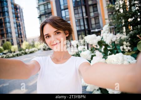 Photo de joyeuse belle fille mignonne habillée de vêtements élégants enregistrant une vidéo faisant du contenu de blog instagram à l'extérieur Banque D'Images