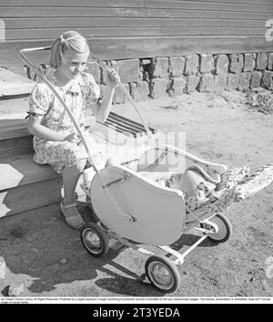 L'été dans les années 1940 Une fille est assise sur les escaliers balançant un landau où son petit frère est couché. Elle porte une robe d'été pour être belle, mais ses chaussures sont très usées. Suède 1947. Kristoffersson réf. V93-5 Banque D'Images