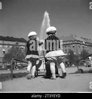 Pour une promenade dans les années 1940 Deux petits enfants jouent dans le parc en poussant des landaus de poupée. Ils portent presque les mêmes vêtements, des vestes noires à rayures blanches et un béret blanc. Suède mai 1940 Kristoffersson ref 133-12 Banque D'Images