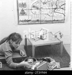 Femme au gramophone dans les années 1950 Une adolescente typique des années 1950 couchée sur le sol écoutant de la musique d'un petit gramophone. Elle joue le genre de disques appelés singles. Enregistrement contenant généralement un enregistrement de moins de pistes qu'un enregistrement LP. Ce disque unique a été joué à la vitesse de 45 tours par minute (tours par minute) et était de 7 pouces de diamètre, 17,8 cm. Le premier single est publié le 31 mars 1949 par RCA Victor. Suède 1959. Réf. SSMSAX000521L Banque D'Images