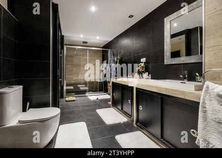 Grande salle de bains entièrement carrelée avec carrelage noir en ardoise, meuble-lavabo en bois noir, comptoir en marbre Banque D'Images
