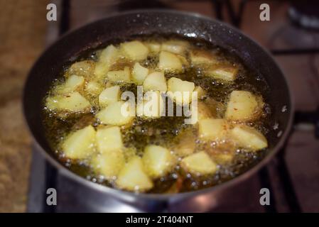 Mise au point sélective sur une poêle à frire cuisant des frites. Frire des pommes de terre dorées dans de l'huile chaude sur la cuisinière Banque D'Images