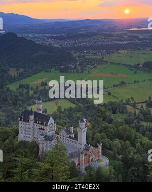 Vue aérienne du château de Neuschwanstein au coucher du soleil avec ciel orange et soleil en arrière-plan Banque D'Images