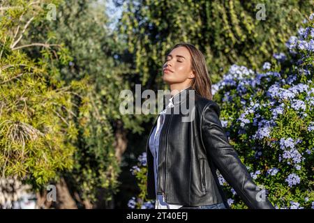 Jeune femme aux yeux fermés 20 ans caucasien seul dans le parc respirant de l'air frais par une journée ensoleillée Banque D'Images