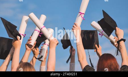 Les diplômés de l'université lèvent la main avec des casquettes et des diplômes au ciel. Banque D'Images