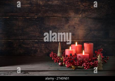 Troisième couronne de l'AVENT avec des bougies rouges, trois sont allumées, décoration avec des baies, des boules de Noël et de petits arbres en bois, fond rustique foncé, copie spa Banque D'Images