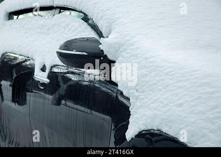 rétroviseur avec clignotant, voiture noire couverte de neige par une froide journée d'hiver, gros plan d'un véhicule bloqué par les précipitations, personne. Banque D'Images