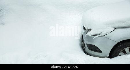 une voiture garée près d'une dérive de neige couverte d'un tas de neige sur le capot et bloquée par les précipitations par une froide journée d'hiver. Banque D'Images