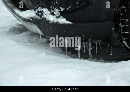 voiture garée noire couverte de glaçons sur le pare-chocs par une journée froide d'hiver, gros plan d'un véhicule et de glace avec de la neige, personne. Banque D'Images