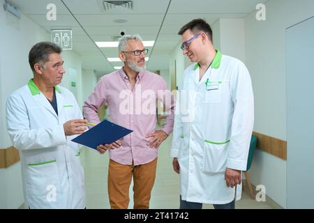 Trois hommes, deux médecins et un homme âgé, marchent le long du couloir de l'hôpital Banque D'Images