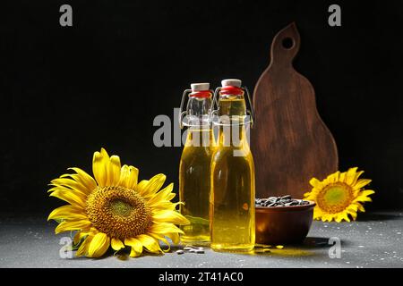 Bouteilles d'huile de tournesol et bol avec des graines sur fond noir Banque D'Images