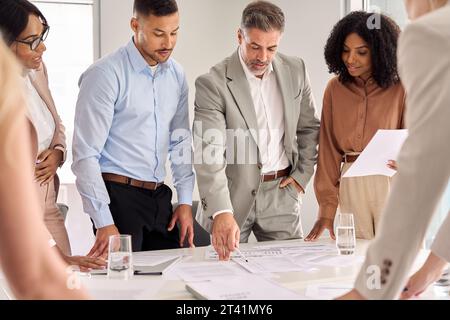 Les membres de l'équipe d'affaires travaillant sur le plan du projet se tiennent debout à la réunion de bureau de table. Banque D'Images