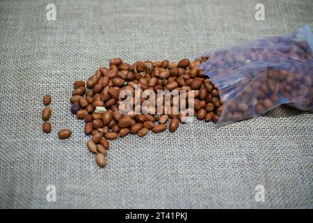un tas de cacahuètes crues vient de sortir d'un sac en plastique avec un sac en toile de jute en arrière-plan Banque D'Images