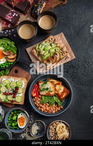 Nourriture savoureuse avec pain grillé d'avocat, légumes, œufs sur fond sombre. Concept de petit déjeuner Helthy. Espace de copie. Banque D'Images